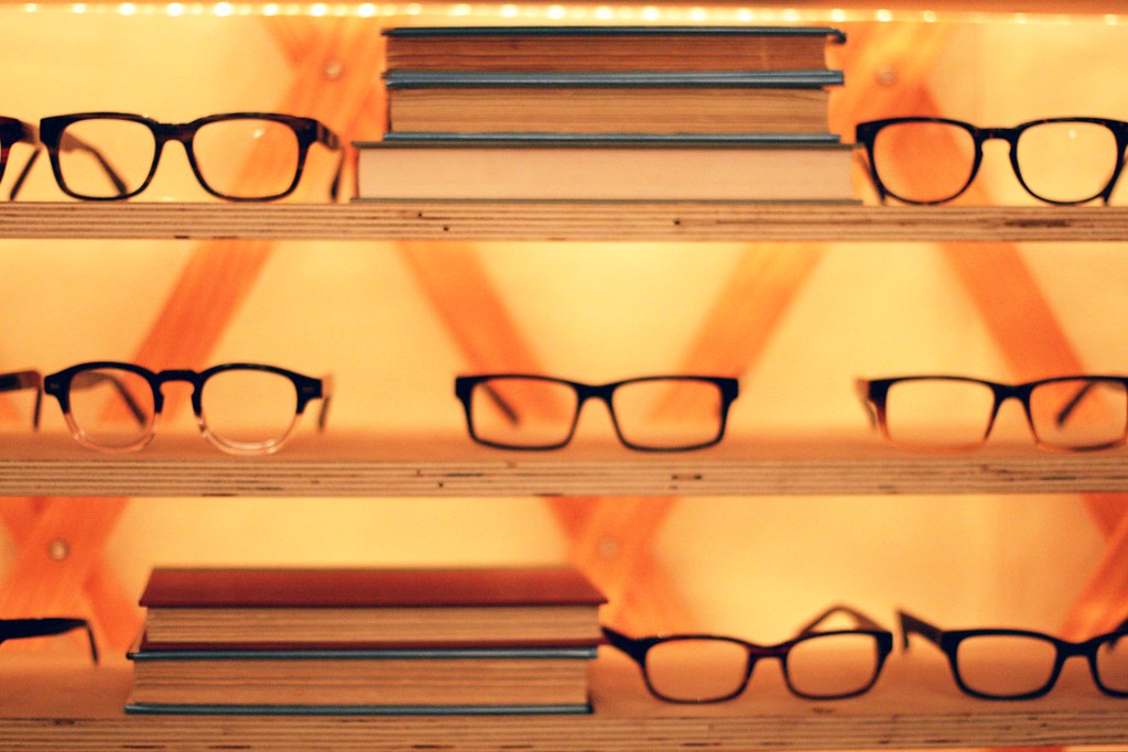 reading glasses on a shelf with stacks of books with an orange background