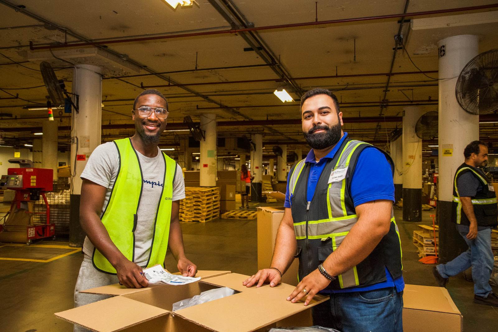 Two smiling warehouse employees unbox a package